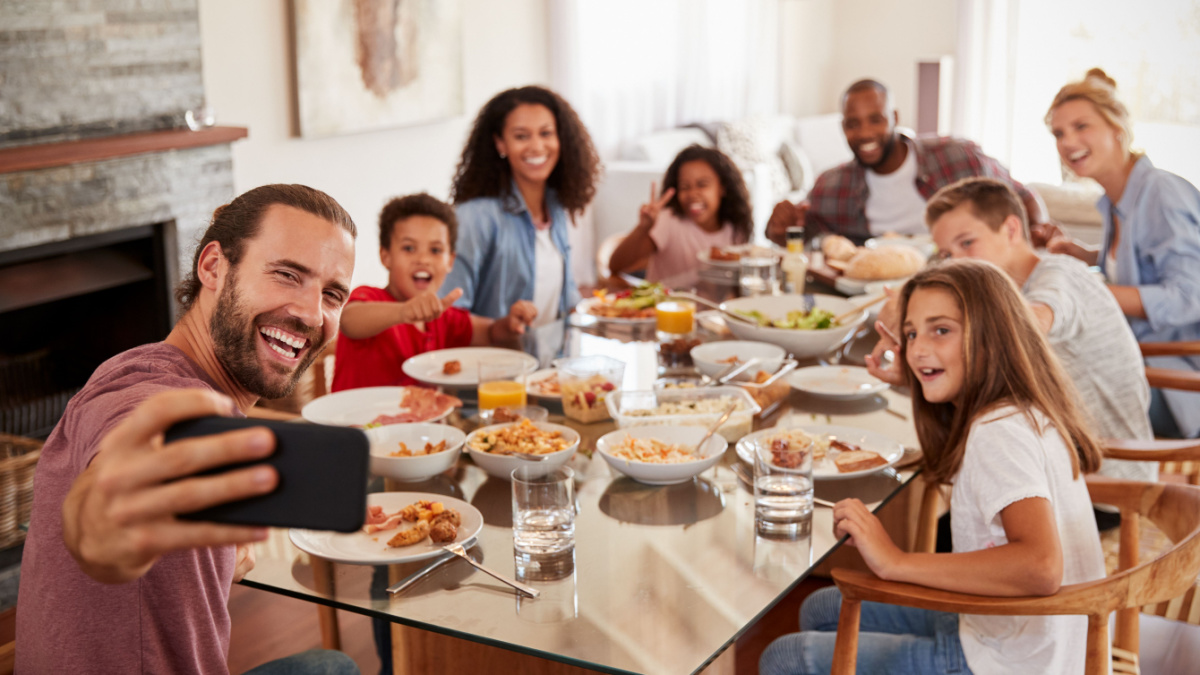 Two Families Taking Selfie As They Enjoy Meal At Home Together.