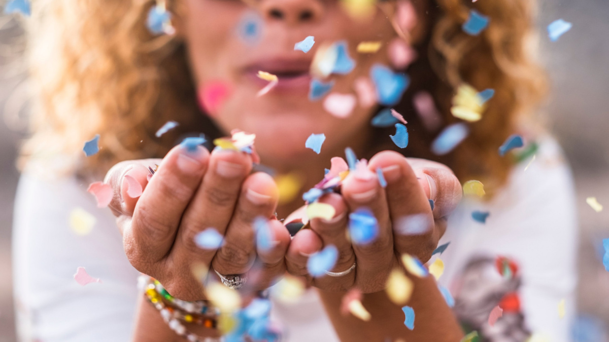 beautiful defocused woman blow confetti from hands. celebration and event concept. happiness and coloured image. movement and happiness having fun.