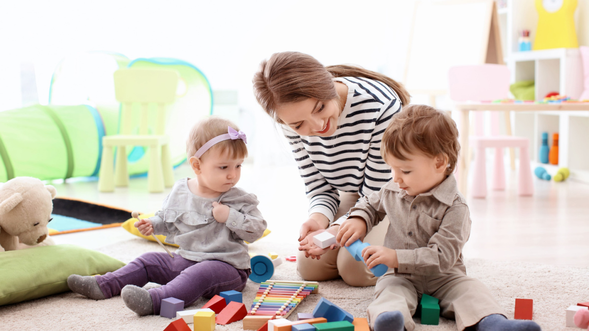 Young nanny playing with little children, indoors.