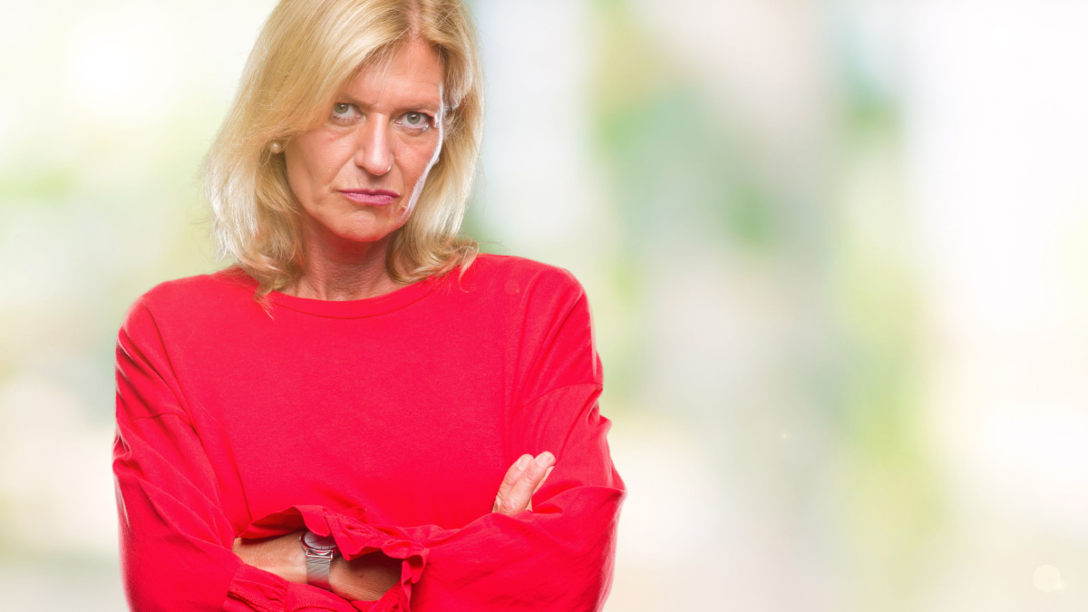 Middle age blonde woman over isolated background skeptic and nervous, disapproving expression on face with crossed arms.