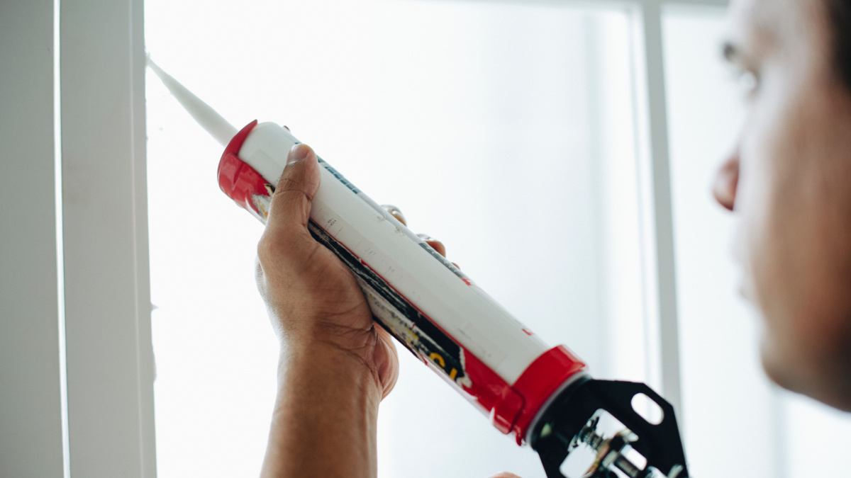 Man using a silicone gun to repair a window.