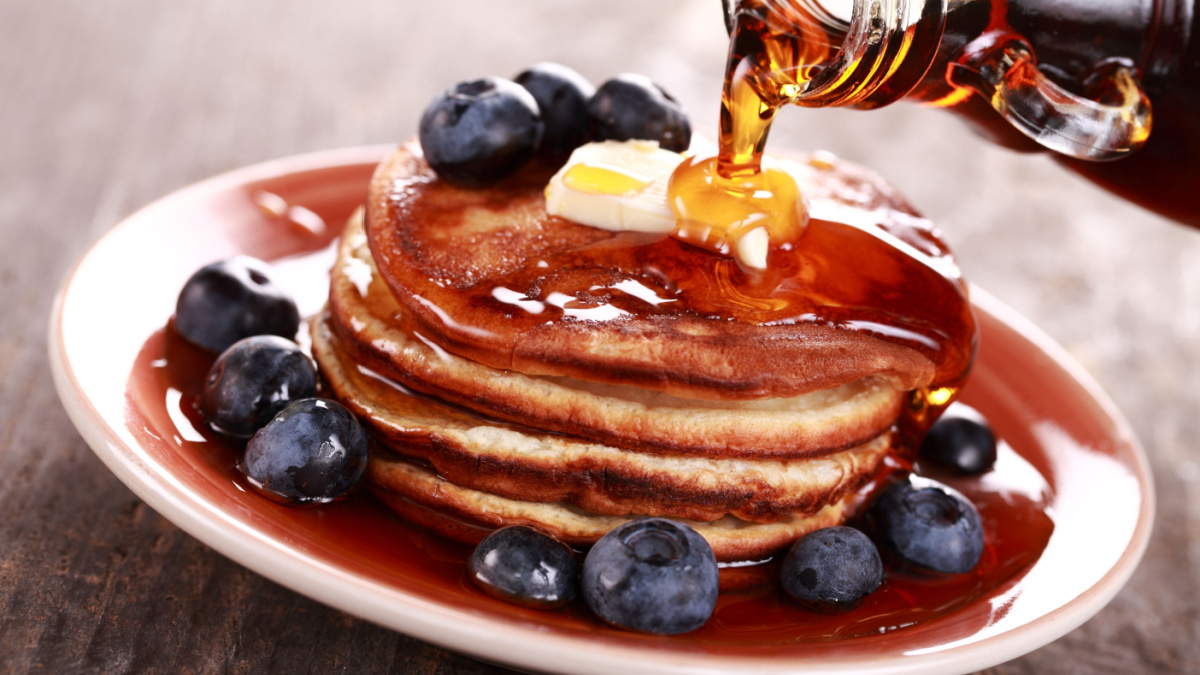 Pouring maple syrup on stack of pancakes.