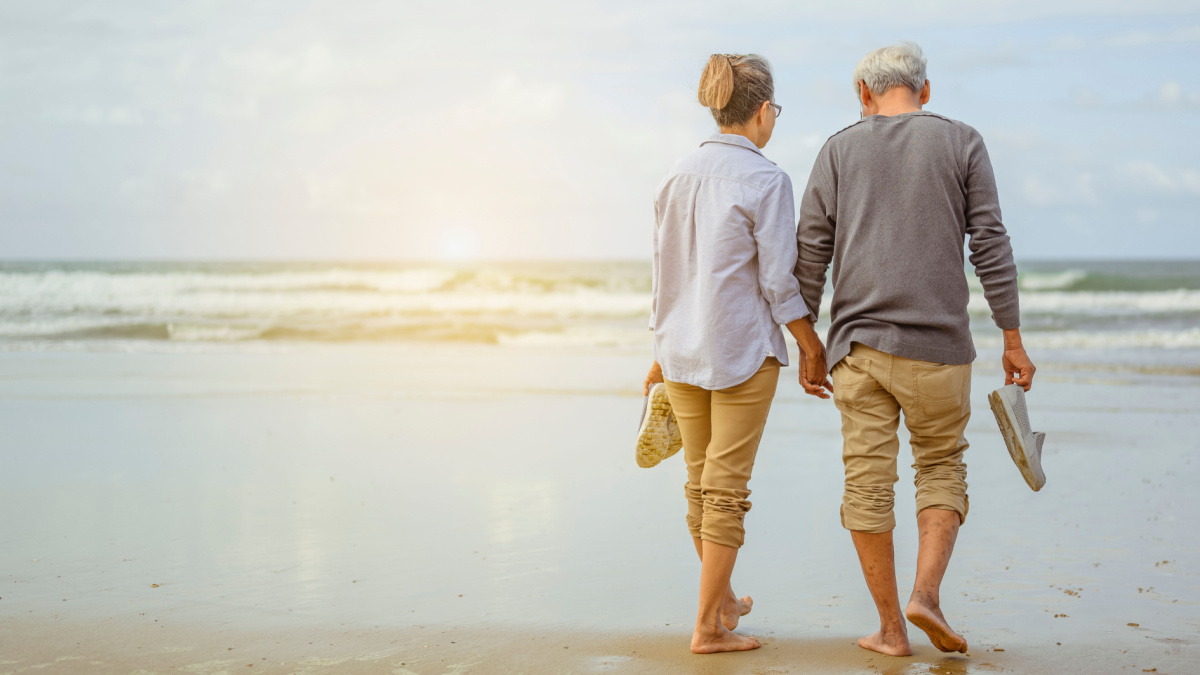 Senior couple walking on the beach holding hands at sunrise, plan life insurance at retirement concept.