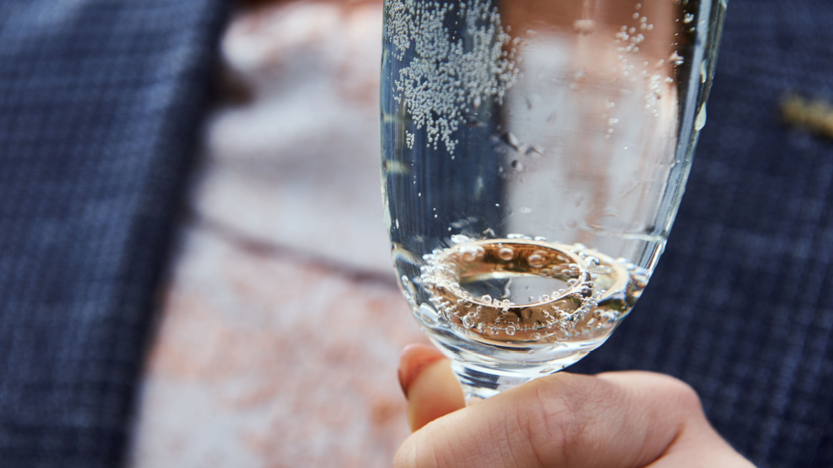 Champagne cup with wedding rings in girl's hand. Wedding rings in champagne glass.