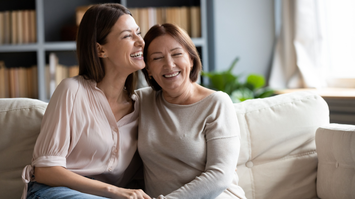 Happy senior mother and grownup daughter sit relax on couch in living room talk laugh and joke, smiling overjoyed middle-aged mom and adult girl child rest at home have fun enjoying weekend together.