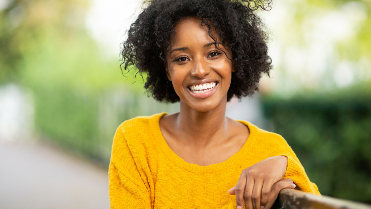Close up portrait of beautiful young black woman sitting on bench outside and smiling.