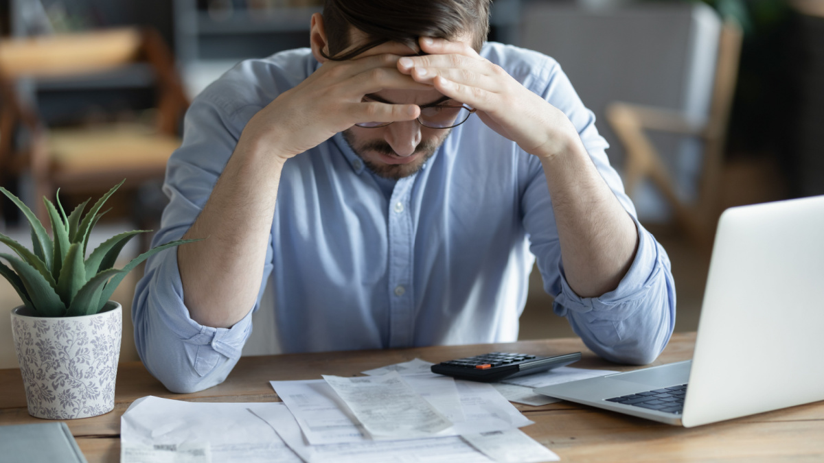 Sad depressed man checking bills, anxiety about debt or bankruptcy, financial problem, bank debt or lack of money, unhappy frustrated young male sitting at work desk with laptop and calculator.