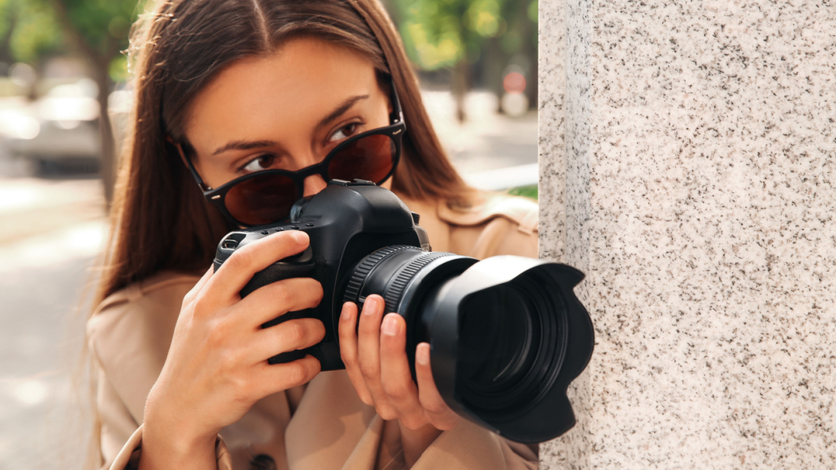 Private detective with camera spying near building on city street.