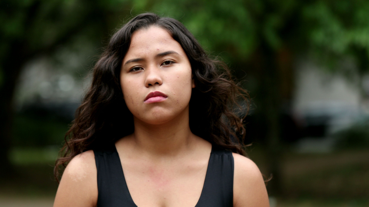 Hispanic girl standing outside looking at camera. Latina young woman serious expression.