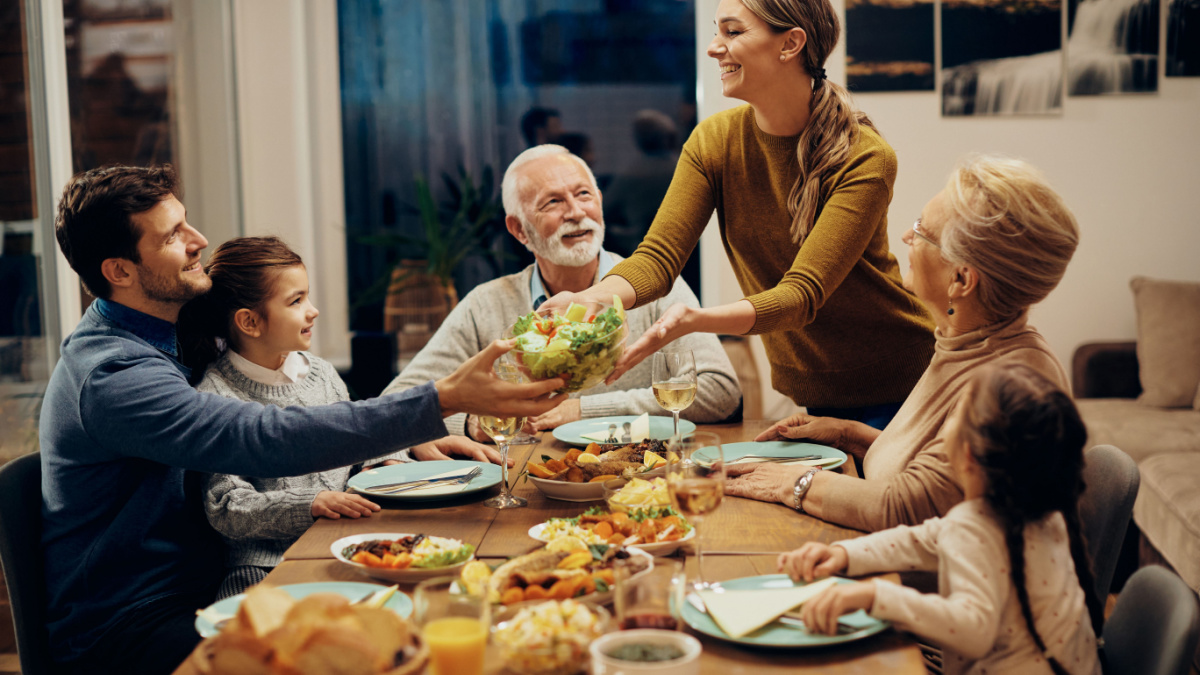 Happy multi-generation family enjoying in a lunch together at home. Focus is on young woman serving salad at dining table.