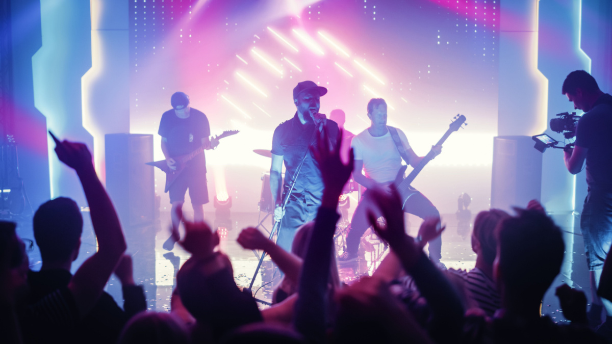Rock Band with Guitarists and Drummer Performing at a Concert in a Night Club. Front Row Crowd is Partying.