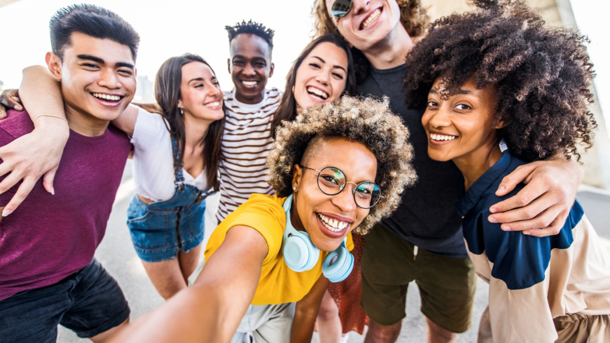 Multicultural happy friends having fun taking group selfie portrait on city street .