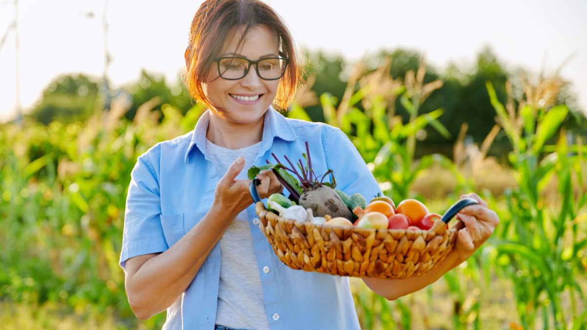 Middle-aged woman gardener farmer with basket of ripe vegetables.