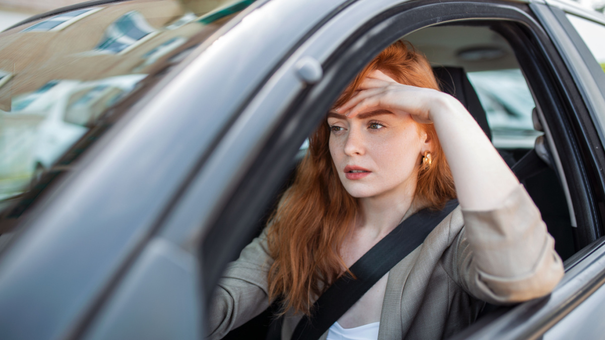 Nervous female driver sits at wheel, has worried expression as afraid to drive car by herself for first time.