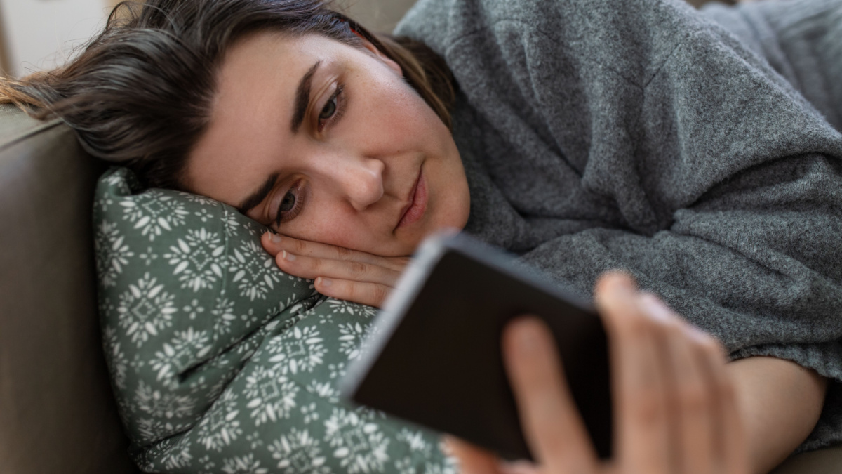 mental health, psychological help and depression concept - stressed woman with smartphone lying on sofa at home.