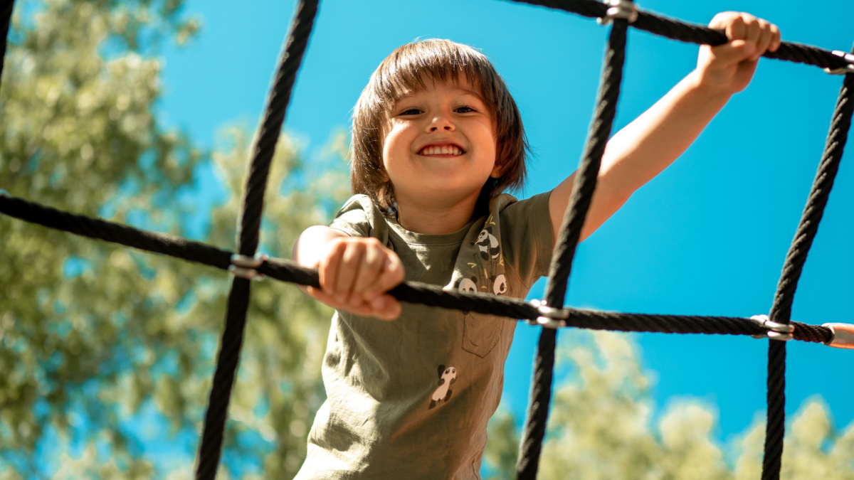 A child climbs up an alpine grid in a park on a playground on a hot summer day. children's playground in a public park, entertainment and recreation for children, mountaineering training.