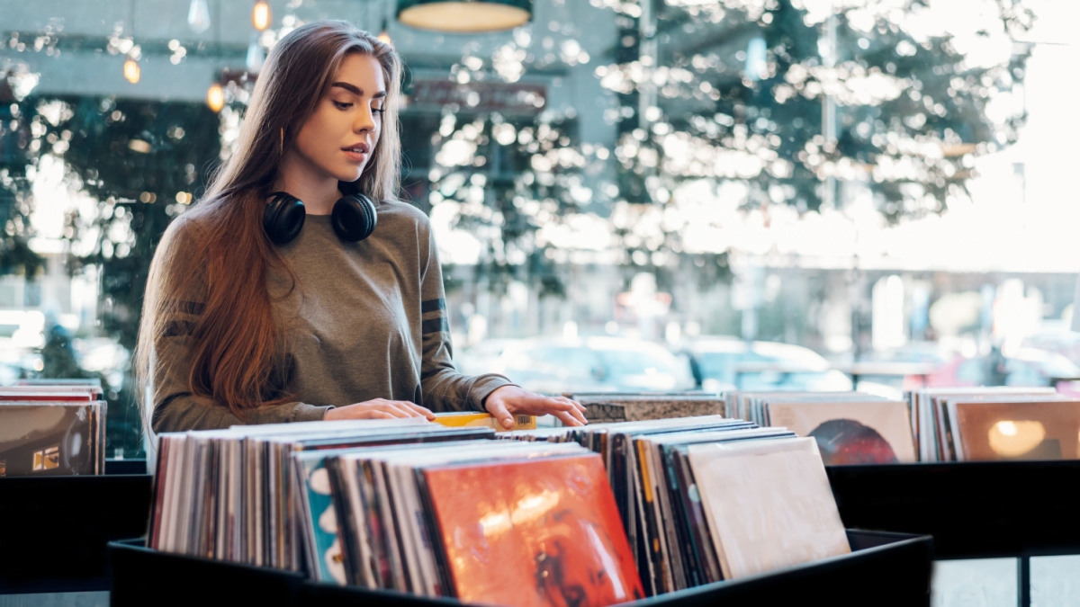 Portrait of a beautiful young woman with a headphones around her neck browsing records in the vinyl record store.