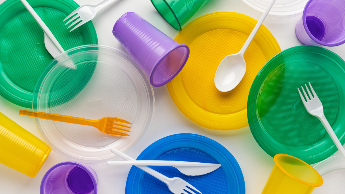 Multi-colored disposable plastic tableware on a light background, studio shot, close-up.