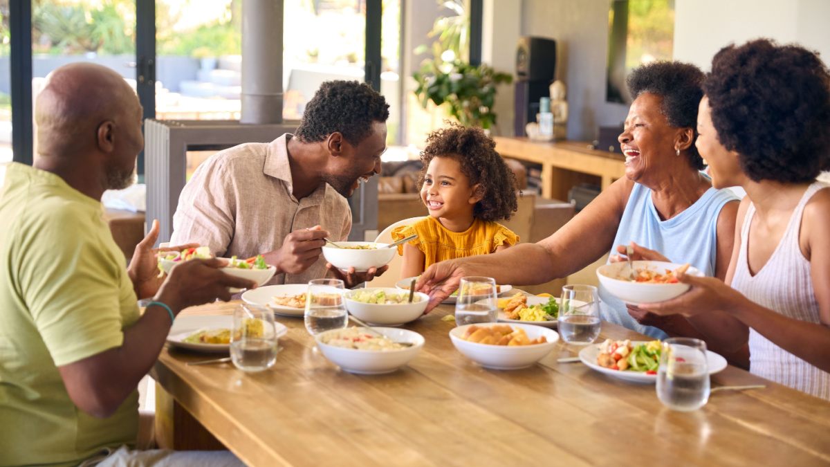 Multi-Generation Family Sitting Around Table Serving Food For Meal At Home.