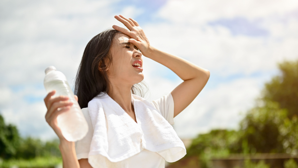 An exhausted and sweaty young Asian woman in sportswear is fighting the heat wave while running in a park on a sunny summer day. summer activity, heat stroke, dehydrated.