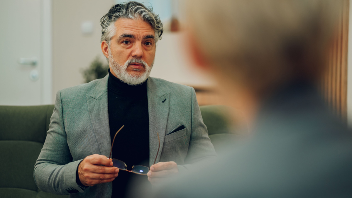 A serious senior client is sitting in a doctor's office and discussing problems with a psychotherapist in a session. An anxious man is getting professional help and support in session with a shrink.