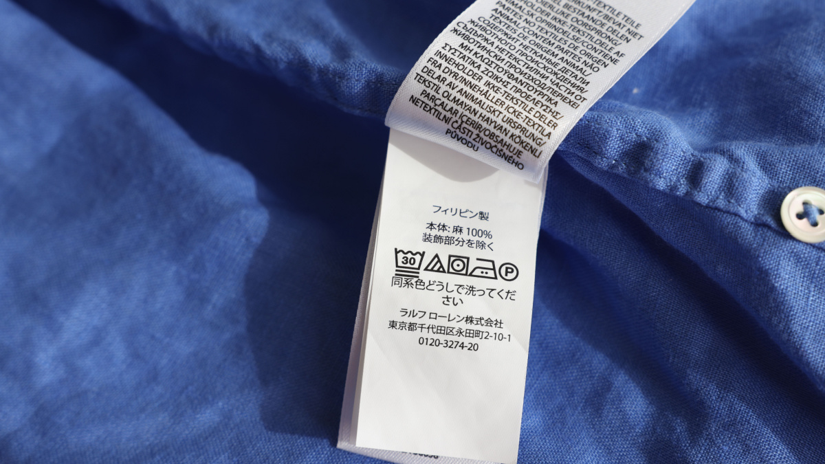 Clothing label in different languages on blue garment, closeup.