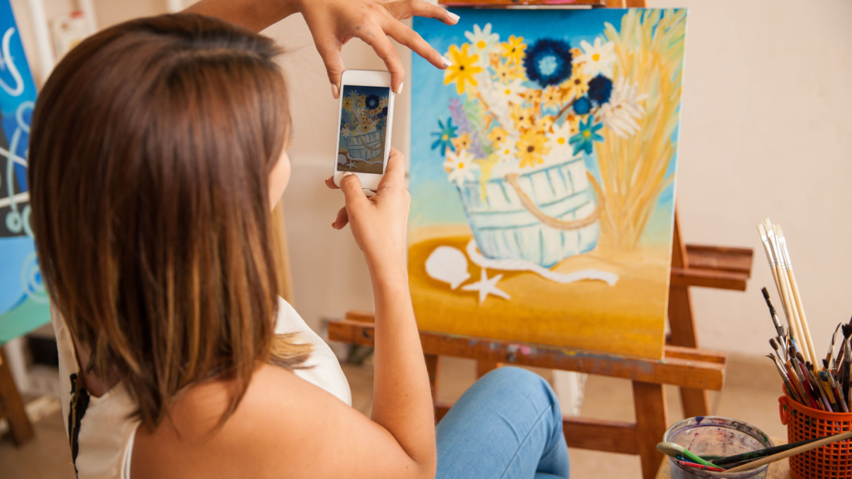 Rear view of a young woman taking a photo of her most recent painting to share it and sell it online.
