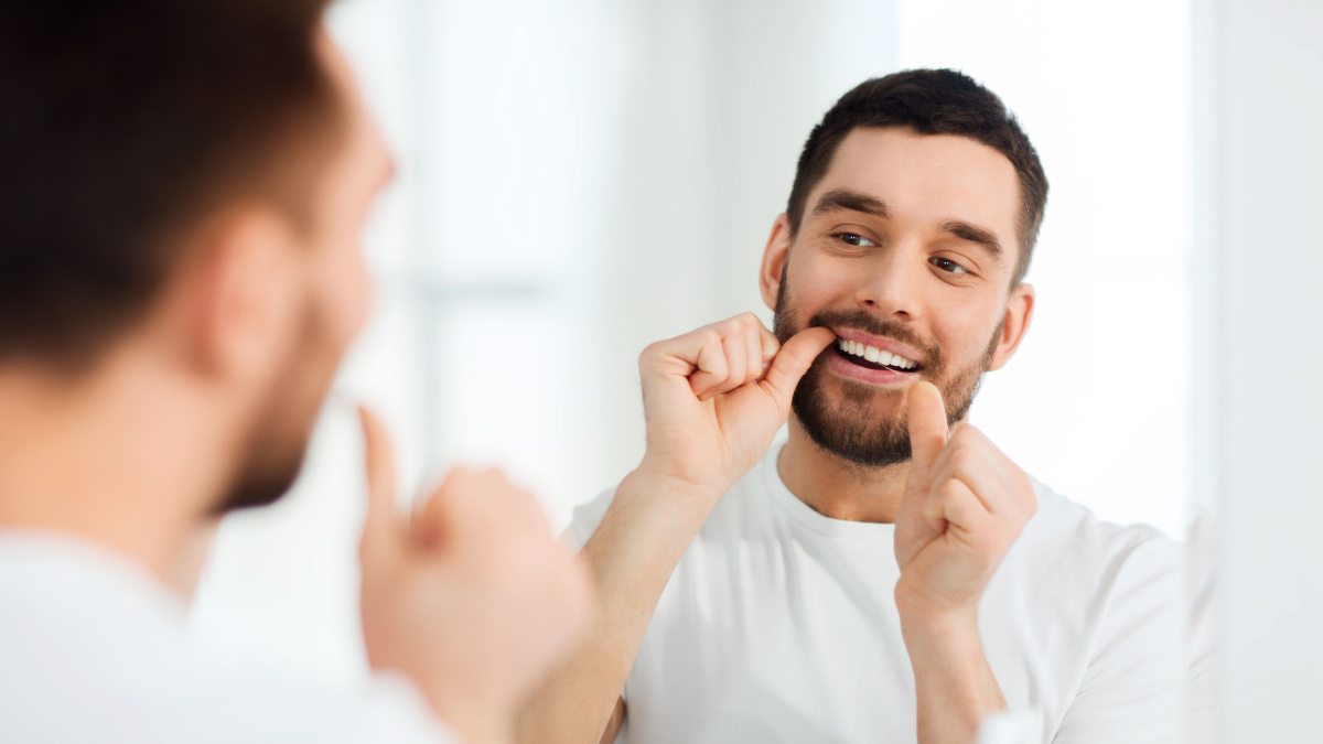 man with dental floss cleaning teeth at bathroom