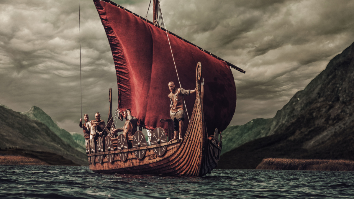 Group of vikings are floating on the sea on Drakkar with mountains on the background.