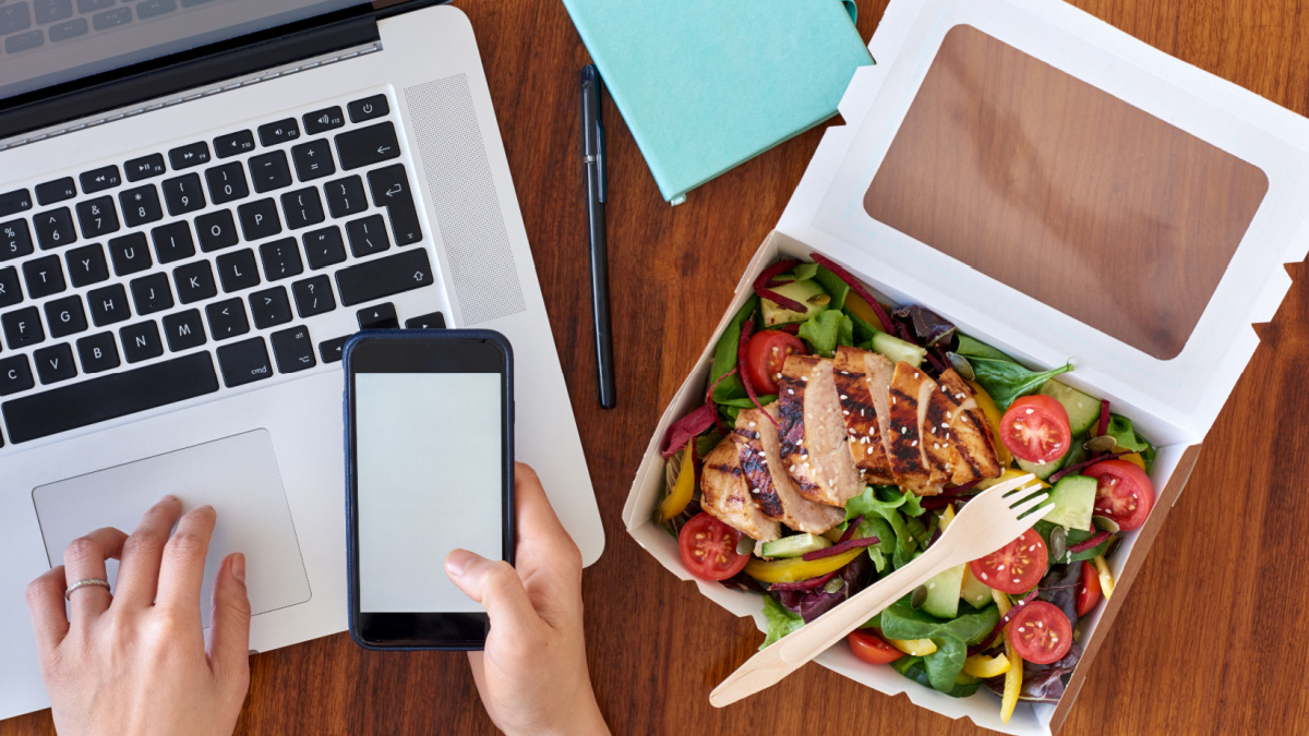 Hands working on laptop computer and ordering food on mobile cell phone app application.