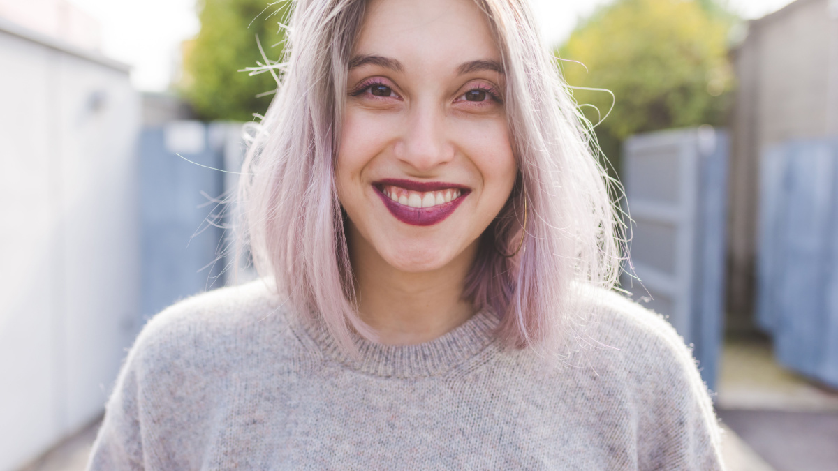 Portrait of young beautiful caucasian purple grey hair woman outdoor in the city looking at camera, smiling - happiness, carefree, serene concept.