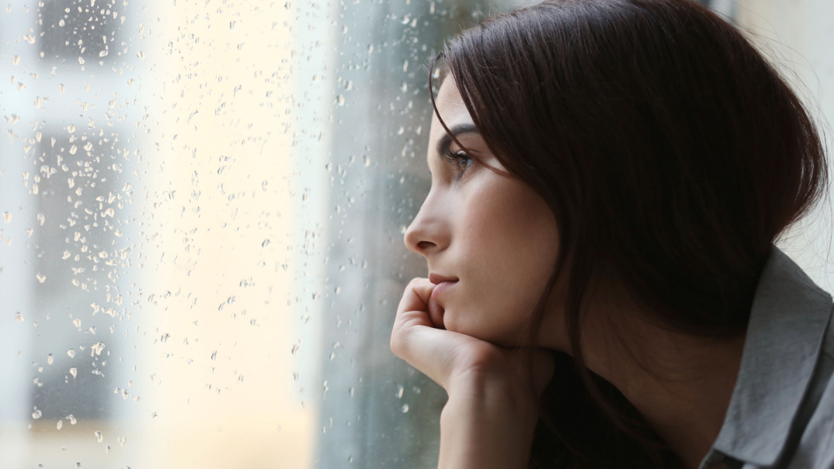 Depressed young woman near window at home, closeup.