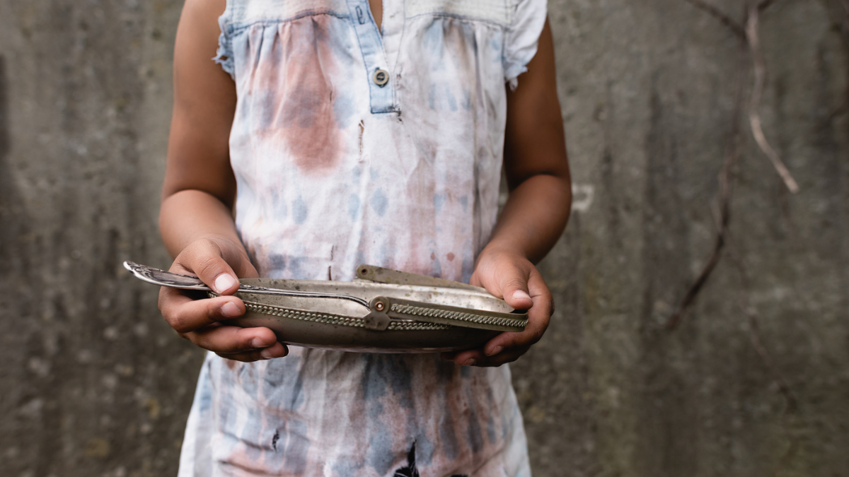 Cropped view of poor african american child in dirty clothes holding metal plate and spoon on urban street.