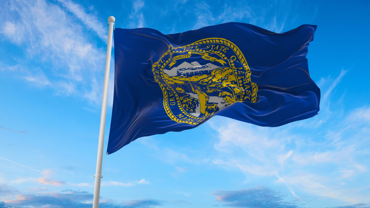 Flag of Nebraska at cloudy sky background on sunset.