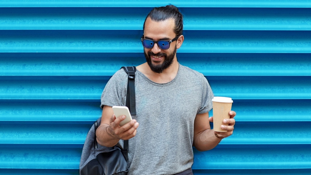 drinks, technology and people concept - close up of man with coffee cup and smartphone on street over ribbed blue wall background.