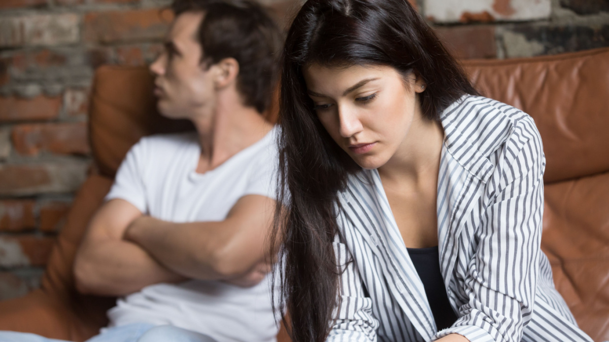 Sad pensive young girl thinking of relationships problems sitting on sofa with offended boyfriend, conflicts in marriage, upset couple after fight dispute, making decision of breaking up get divorced