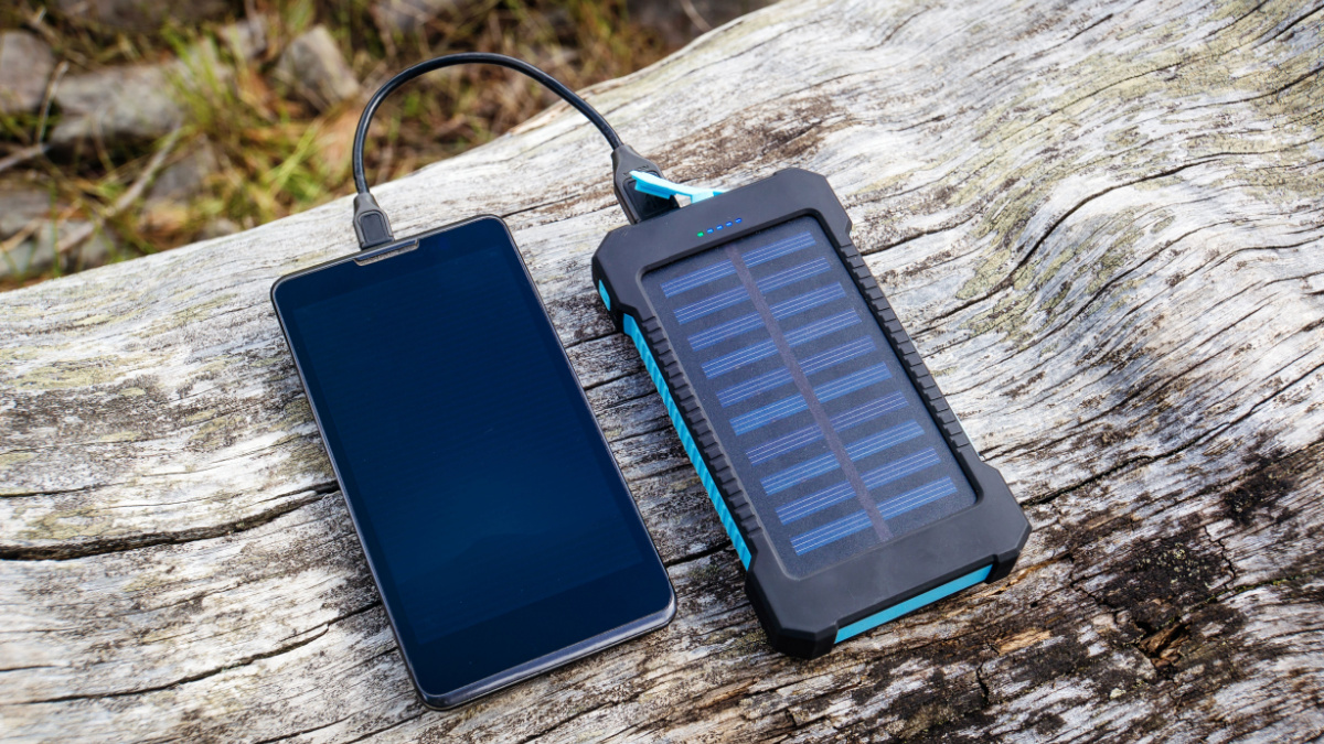 Smartphone charging with pink power bank with solar battery on wood background, selective focus and soft focus
