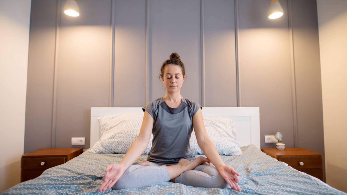 Attractive shape sporty middle aged woman doing seated yoga poses on the bed before sleeping.