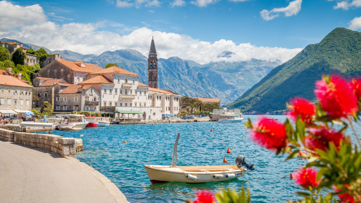 Scenic panorama view of the historic town of Perast at famous Bay of Kotor with blooming flowers on a beautiful sunny day with blue sky and clouds in summer, Montenegro, southern Europe