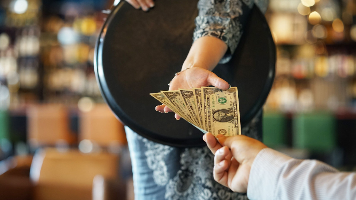 The hand of the waitress takes the tip. The waiter girl receives a tip from the client at the hotel bar.