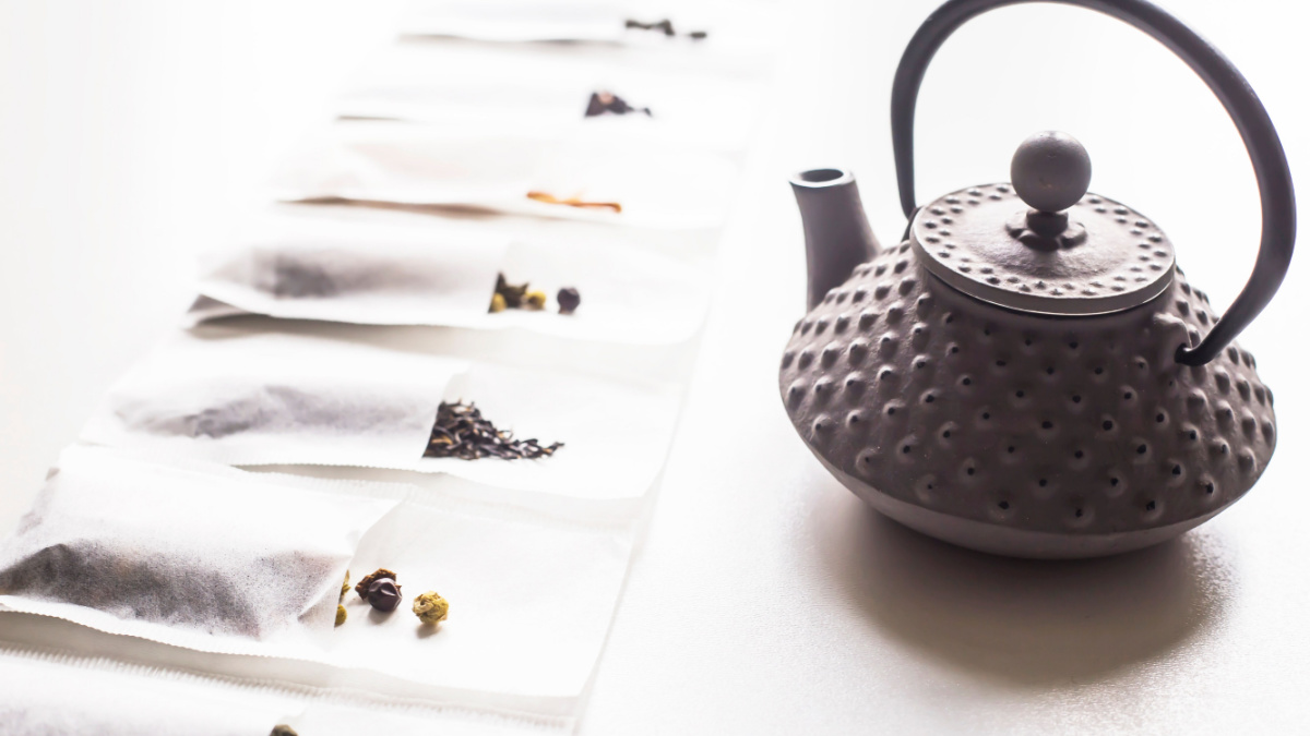 Different teas in a disposable filter bags for brewing next to a gray cast iron kettle on a white background