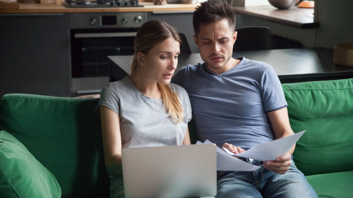 Worried couple confused reading bad news in bank loan documents or money debt calculating high domestic bills or rent payment checking papers with laptop, family discussing financial problems .