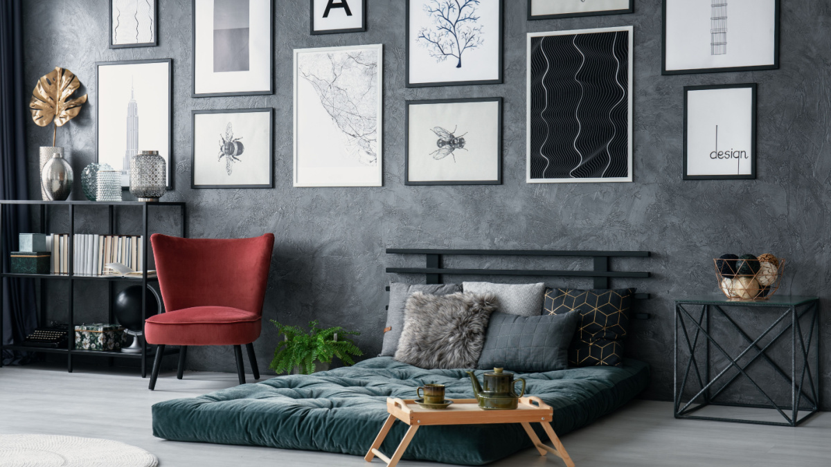 Red armchair next to green mattress in grey bedroom interior with posters on concrete wall.