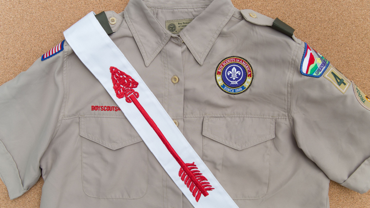 Boy Scouts of America (BSA) uniform shirt and Order of the Arrow sash on a cork brown background