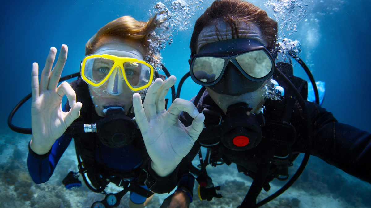 Underwater shoot of a young couple diving with scuba in a tropical sea and showing ok signal.