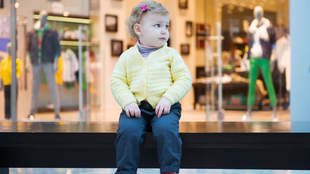 Upset little lost girl sitting on bench in mall