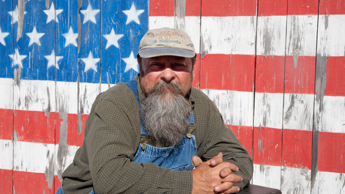 AUGUSTA - JUNE 10: Elderly man poses in front of US flag painted on a barn door on June 10, 2012 near Augusta, Maine.