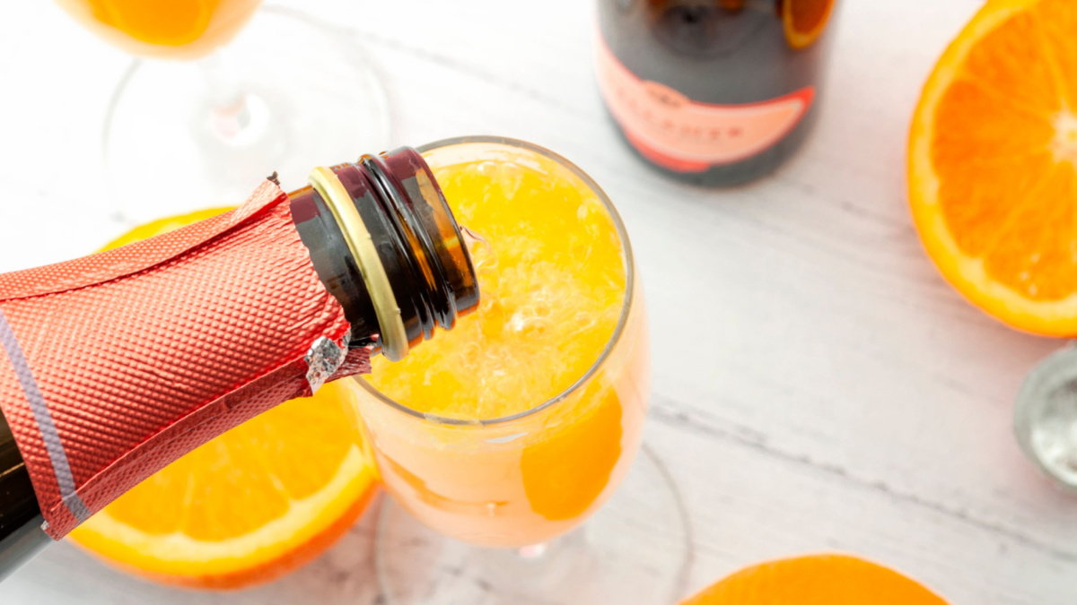Lush mix drinks, summer alcoholic beverages and refreshing brunch mimosa cocktail concept with top view of orange fruits and champagne pouring from bottle of bubbly isolated on wooden table background.