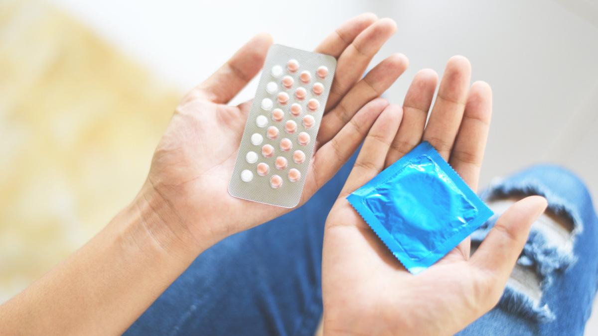 Woman holding contraception pills and condom in hand / Birth control contraceptive means prevent pregnancy or sexually transmitted disease