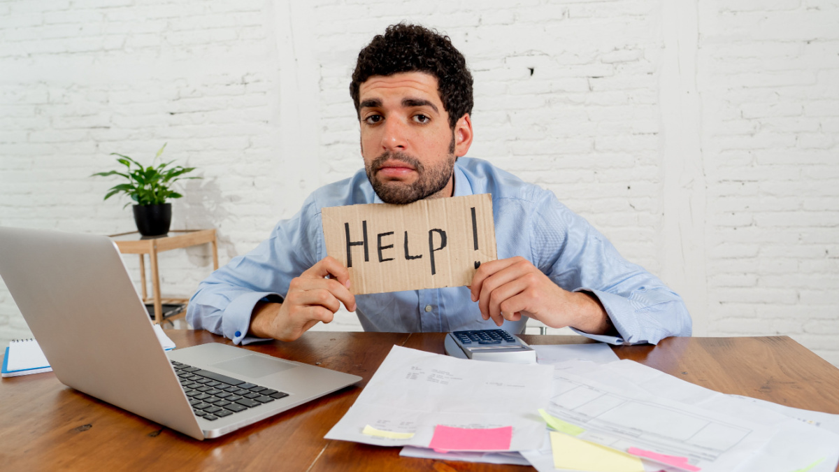Young overwhelmed entrepreneur needing help paying off debts and bills in Small business financial problems. Worried desperate young man feeling stressed working through finances at home office.